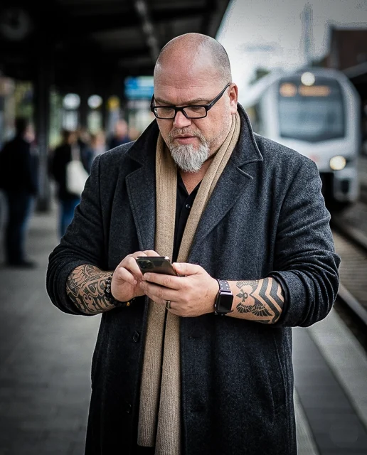 Robert James Perkins mit Brille und Smartphone am Bahnsteig