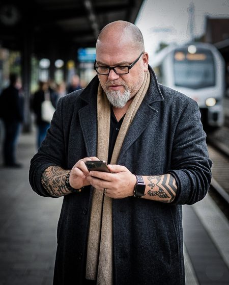 Robert James Perkins mit Brille und Smartphone am Bahnsteig